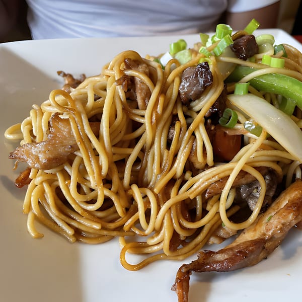 Close-up of Peruvian Lomo Saltado with noodles, beef, onions, and green peppers on a white plate.