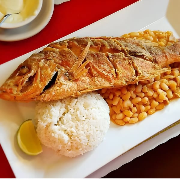 Whole fried fish with white rice, beans, and a lime wedge on a white plate.