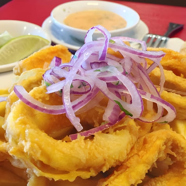 Viva's crispy fried calamari topped with thinly sliced red onions, with lime and sauce in the background.
