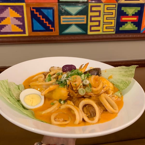 Peruvian seafood dish with shrimp, squid, potatoes, egg, and lettuce in an orange sauce.